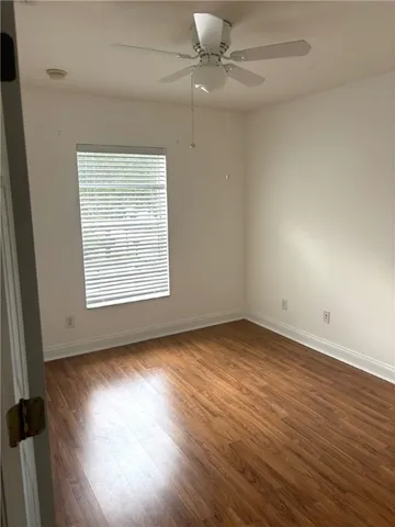 an empty room with wooden floor chandelier fan and windows
