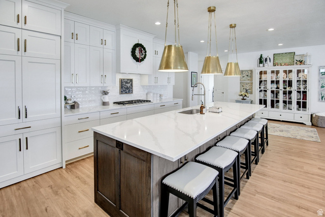 910 South 1700 West Layton, UT 84041 - Photo 5 of 26 Two tone kitchen featuring a kitchen breakfast bar, two tone cabinetry, light stone countertops, a large island, and light wood-style floors