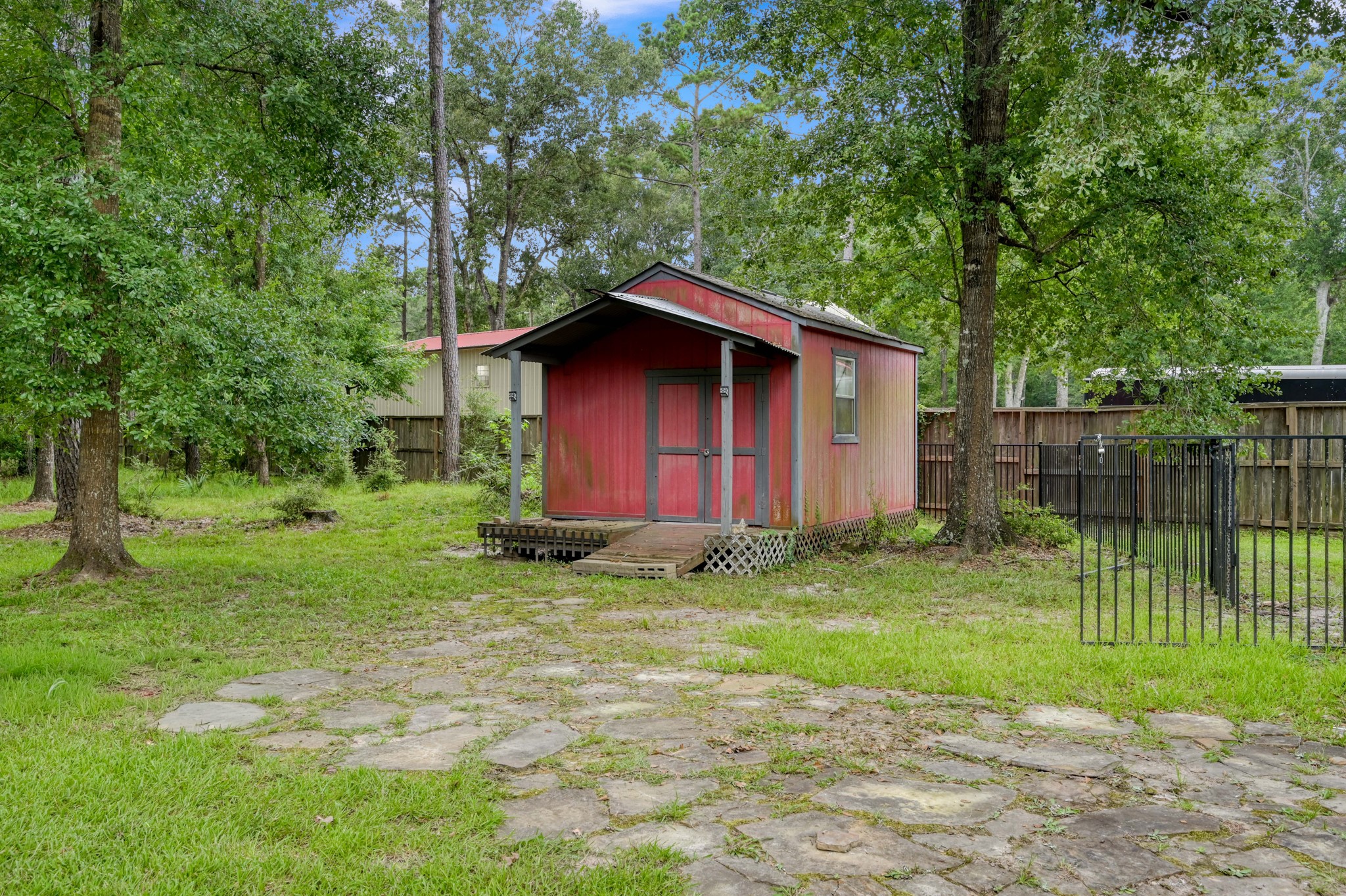 910 Commons Way Court Huffman, TX 77336 - Photo 38 of 49 Charming red shed nestled in a lush, wooded backyard. It features a small porch and is surrounded by a fenced area, offering privacy and potential for various uses.