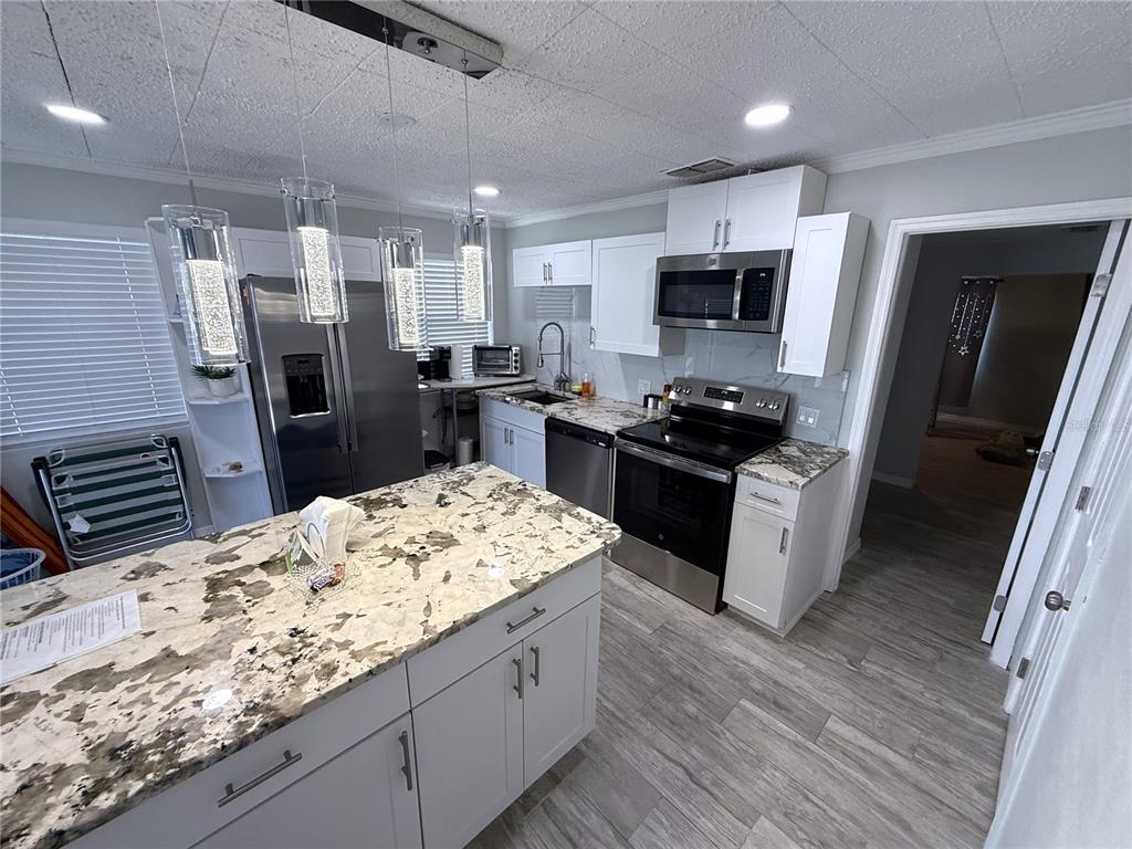 13711 Gulf Boulevard, Unit 1 Madeira Beach, FL 33708 - Photo 28 of 36 a kitchen with stainless steel appliances kitchen island granite countertop a refrigerator a sink a stove top oven and wooden floor