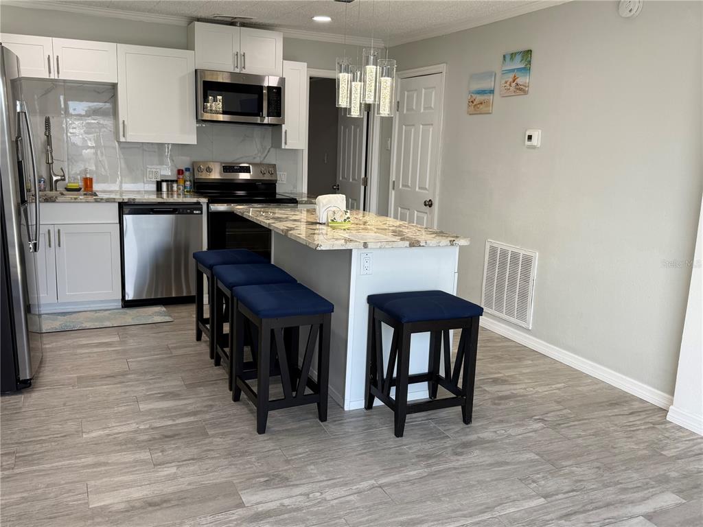 13711 Gulf Boulevard, Unit 1 Madeira Beach, FL 33708 - Photo 33 of 36 a kitchen with stainless steel appliances granite countertop a stove a refrigerator a sink a dining table and chairs with wooden floor