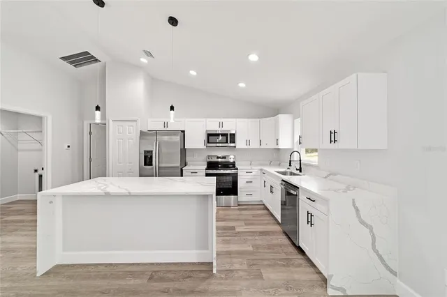 a large kitchen with stainless steel appliances kitchen island a stove a sink a refrigerator and white cabinets