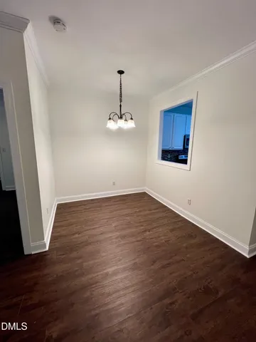 an empty room with wooden floor chandelier and windows