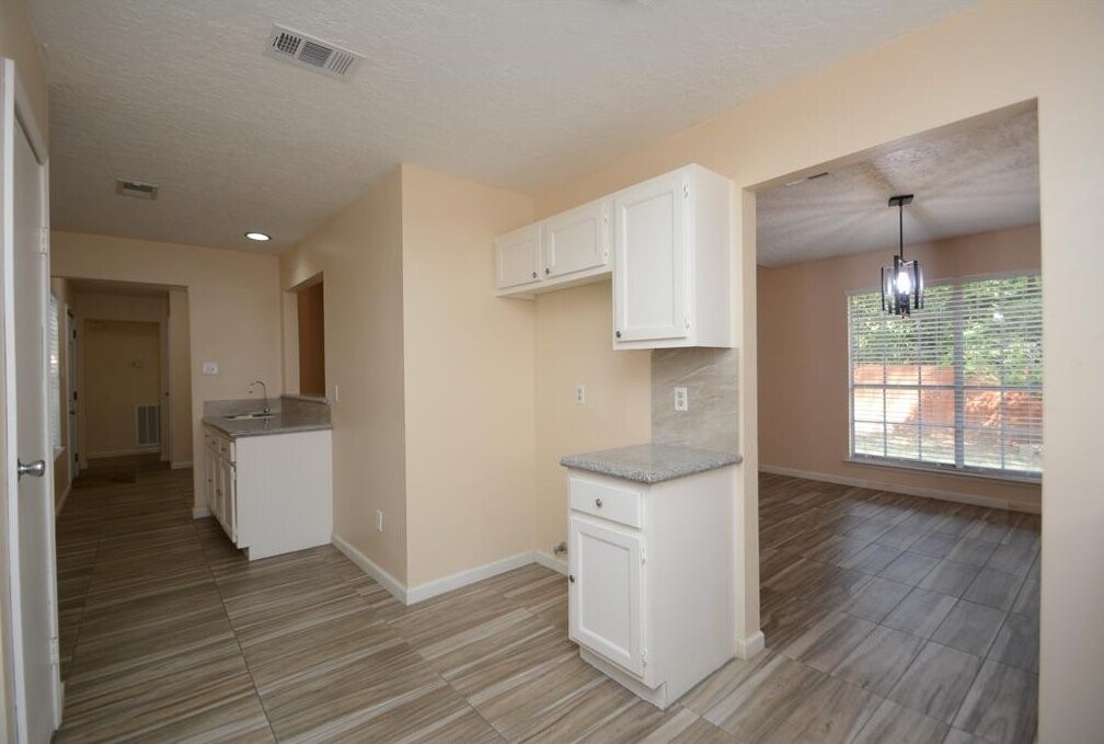 15 South Tallowberry Drive Spring, TX 77381 - Photo 8 of 26 Modern kitchen and dining area with white cabinets, granite countertops, tile flooring, and abundant natural light.