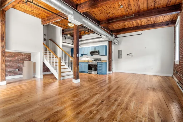 a view of an empty room with wooden floor and stairs