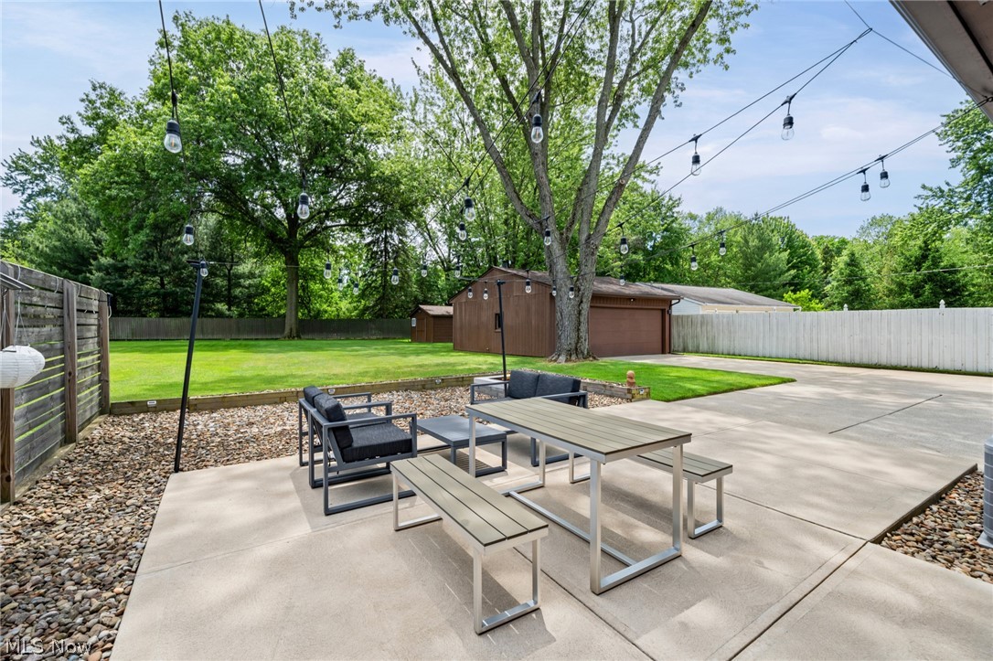 17583 Shurmer Road Strongsville, OH 44136 - Photo 39 of 50 Spacious concrete patio featuring string lighting, a large grassy area, privacy fencing, and mature trees