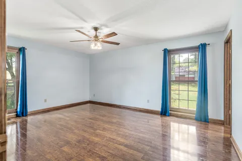 an empty room with wooden floor fan and windows