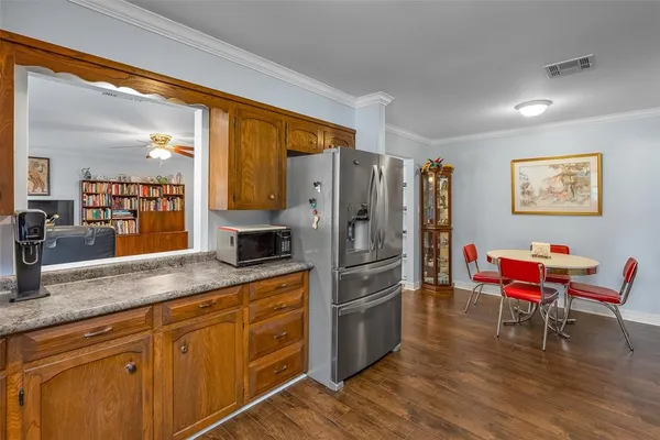 a kitchen with stainless steel appliances granite countertop a refrigerator a sink dishwasher a dining table and chairs with wooden floor