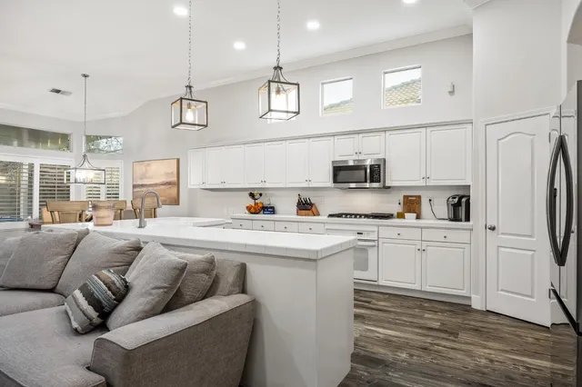 a kitchen with stainless steel appliances granite countertop a refrigerator a stove a sink dishwasher and white cabinets with wooden floor