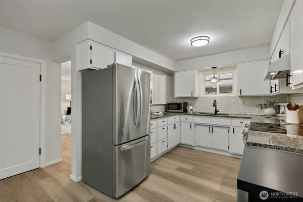 a kitchen with stainless steel appliances granite countertop a refrigerator a stove a sink dishwasher and white cabinets with wooden floor