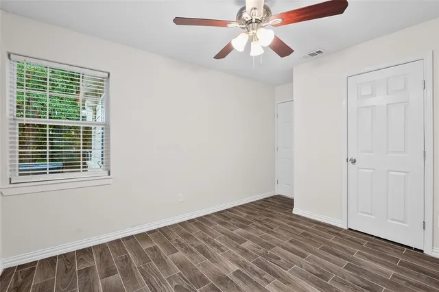an empty room with wooden floor chandelier fan and windows