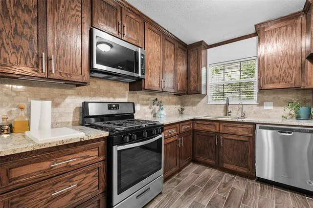 a kitchen with stainless steel appliances granite countertop a refrigerator a stove and a sink with wooden cabinets