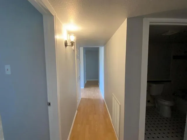 a view of a hallway with wooden floor and a bathroom