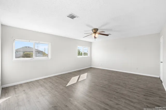 an empty room with wooden floor chandelier fan and windows
