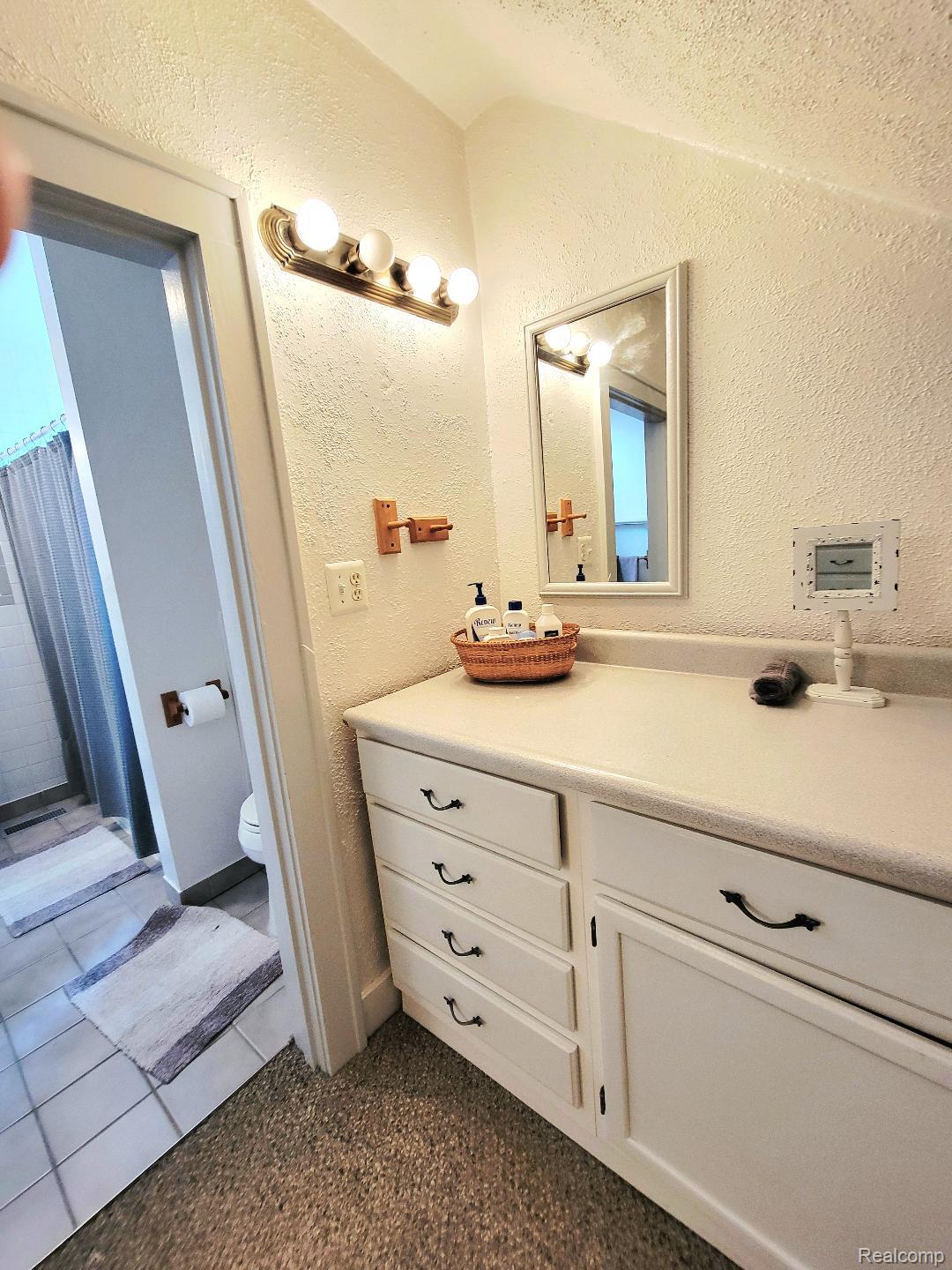 11227 Rivard Avenue Warren, MI 48089 - Photo 29 of 44 Vanity area featuring a built-in white cabinet with black hardware, a light-colored countertop, and a wall-mounted mirror