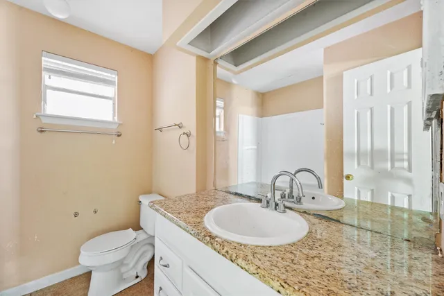 a bathroom with a granite countertop toilet a sink and a mirror