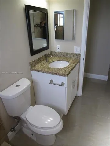 a bathroom with a granite countertop toilet a sink and a mirror