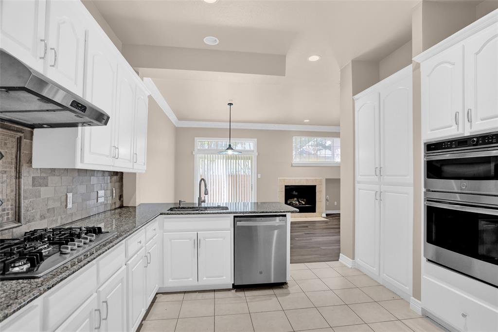 4092 Oberlin Way Addison, TX 75001 - Photo 19 of 40 Kitchen with stainless steel appliances, a sink, under cabinet range hood, a peninsula, and dark stone countertops