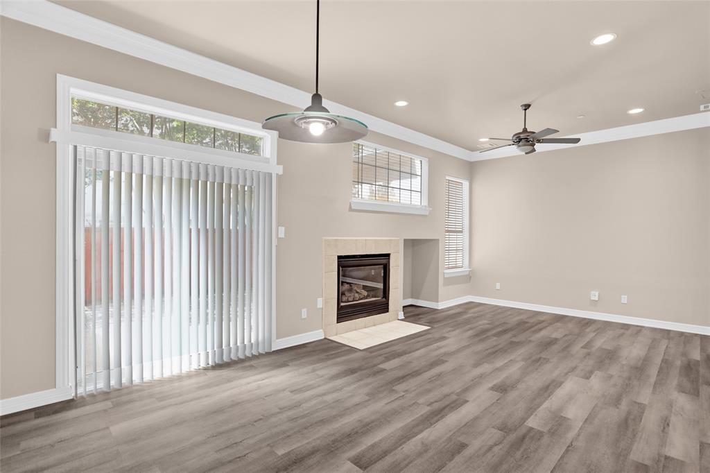4092 Oberlin Way Addison, TX 75001 - Photo 9 of 40 Unfurnished living room with a ceiling fan, healthy amount of natural light, ornamental molding, a tiled fireplace, and wood finished floors