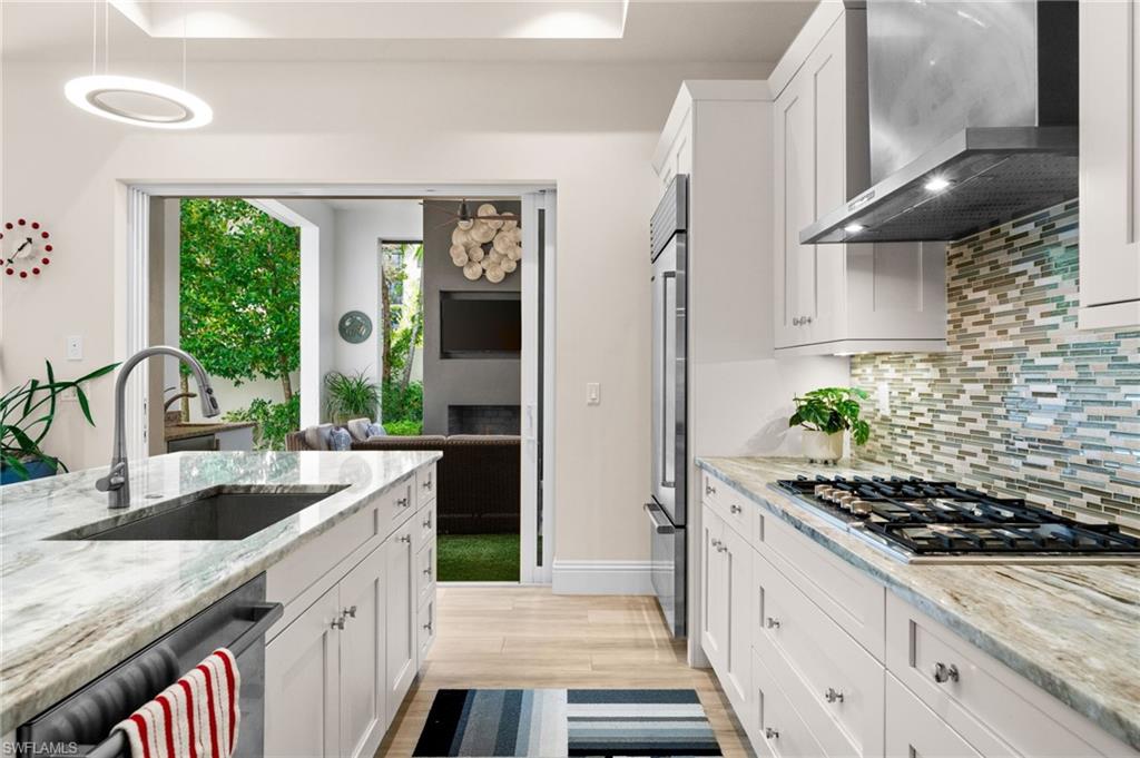9172 Mercato Lane Naples, FL 34108 - Photo 13 of 29 Kitchen with white cabinets, light stone counters, stainless steel appliances, light wood-type flooring, and tasteful backsplash