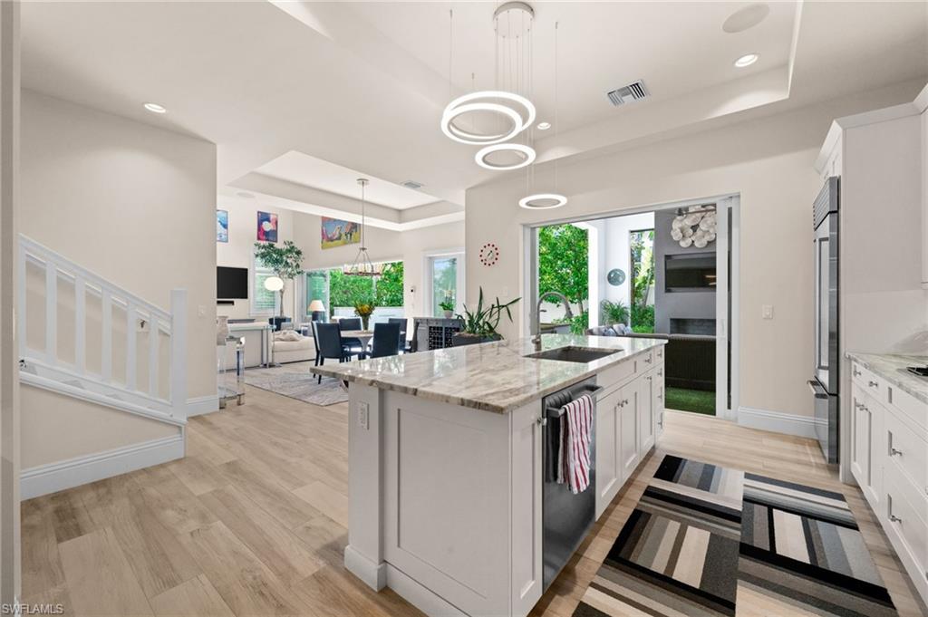 9172 Mercato Lane Naples, FL 34108 - Photo 14 of 29 Kitchen featuring a tray ceiling, white cabinets, light stone countertops, pendant lighting, and an island with sink
