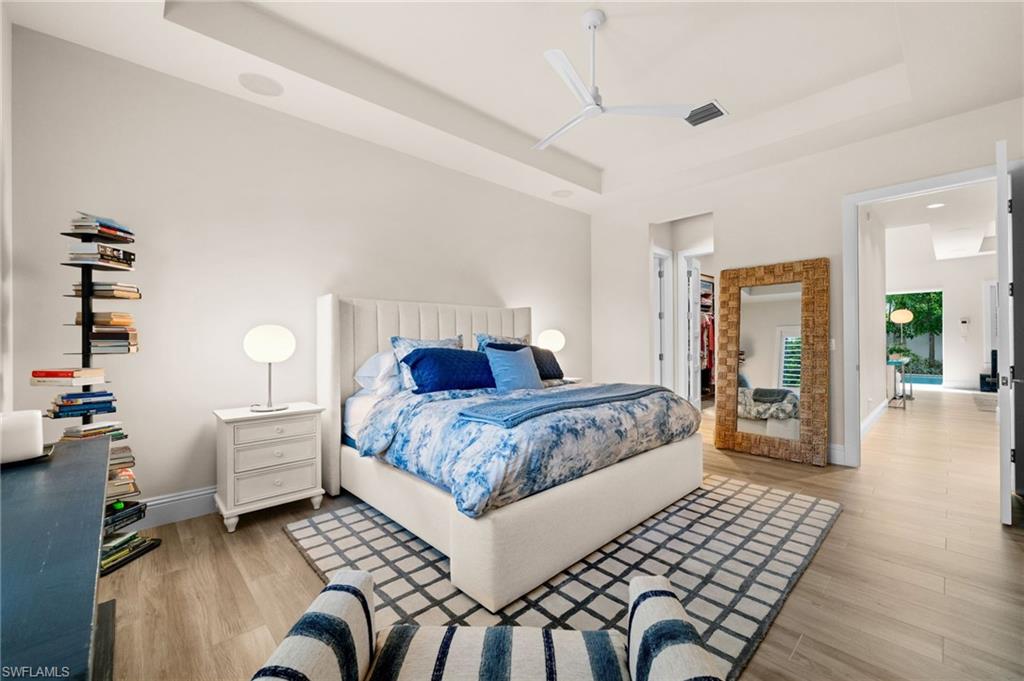 9172 Mercato Lane Naples, FL 34108 - Photo 23 of 29 Bedroom featuring a raised ceiling, light wood-style floors, a walk in closet, and ceiling fan