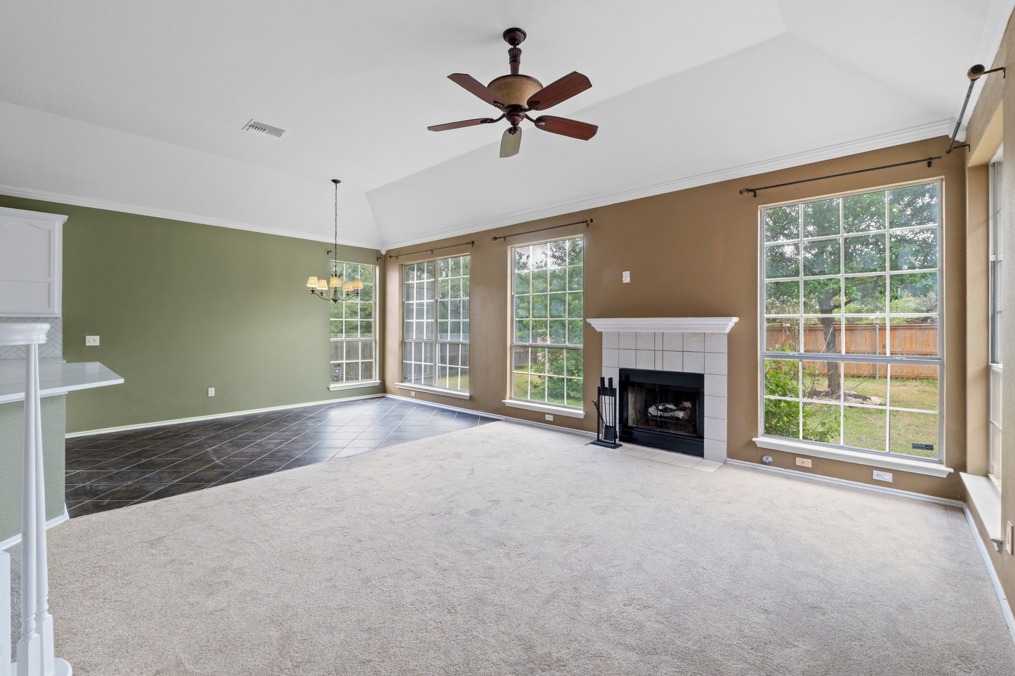 8605 Axis Drive Austin, TX 78749 - Photo 8 of 38 A well-lit living area features a fireplace and a blend of carpet and tile flooring, all beneath a vaulted ceiling with a fan.