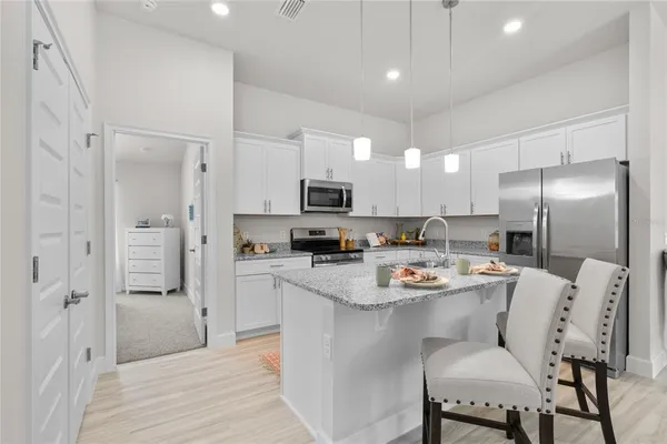 a kitchen with stainless steel appliances a refrigerator a stove a microwave oven a sink with white cabinets and wooden floor