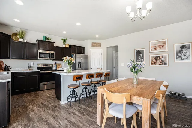 a kitchen with stainless steel appliances granite countertop a stove a refrigerator a kitchen island a dining table and chairs with wooden floor