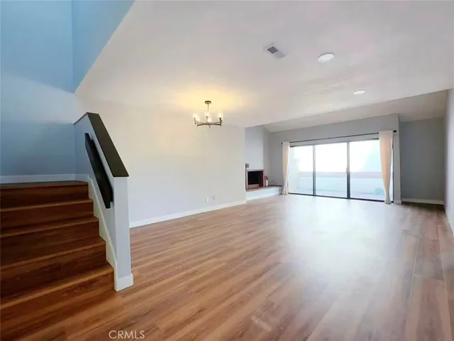 a view of an empty room with wooden floor and fan