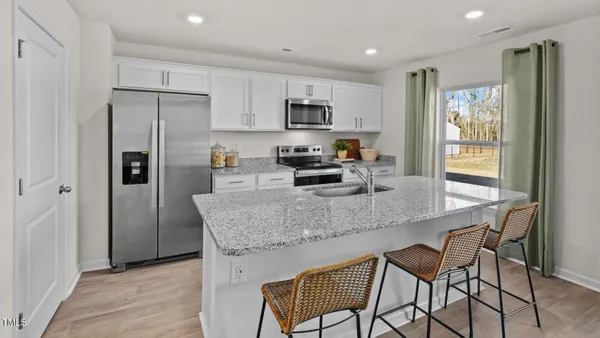 a kitchen with stainless steel appliances granite countertop a dining table chairs refrigerator and sink
