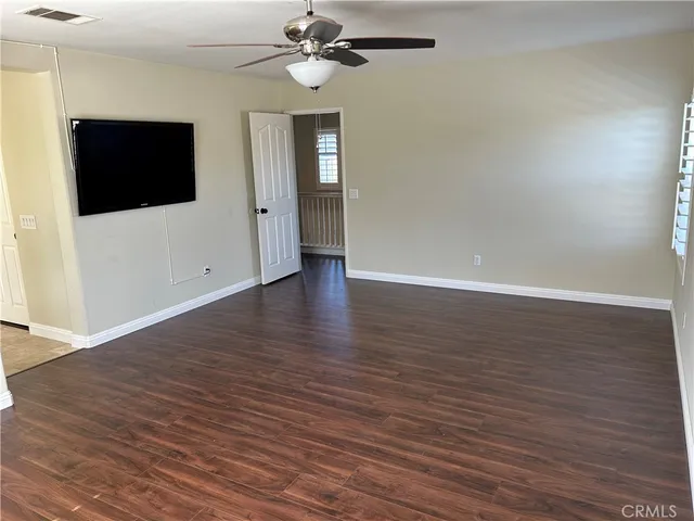 a view of an empty room with wooden floor and a ceiling fan