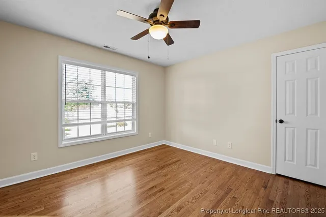 an empty room with wooden floor chandelier fan and windows