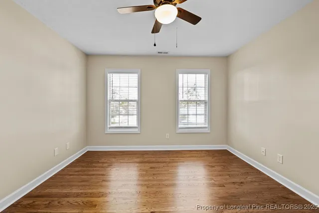 an empty room with wooden floor chandelier fan and windows