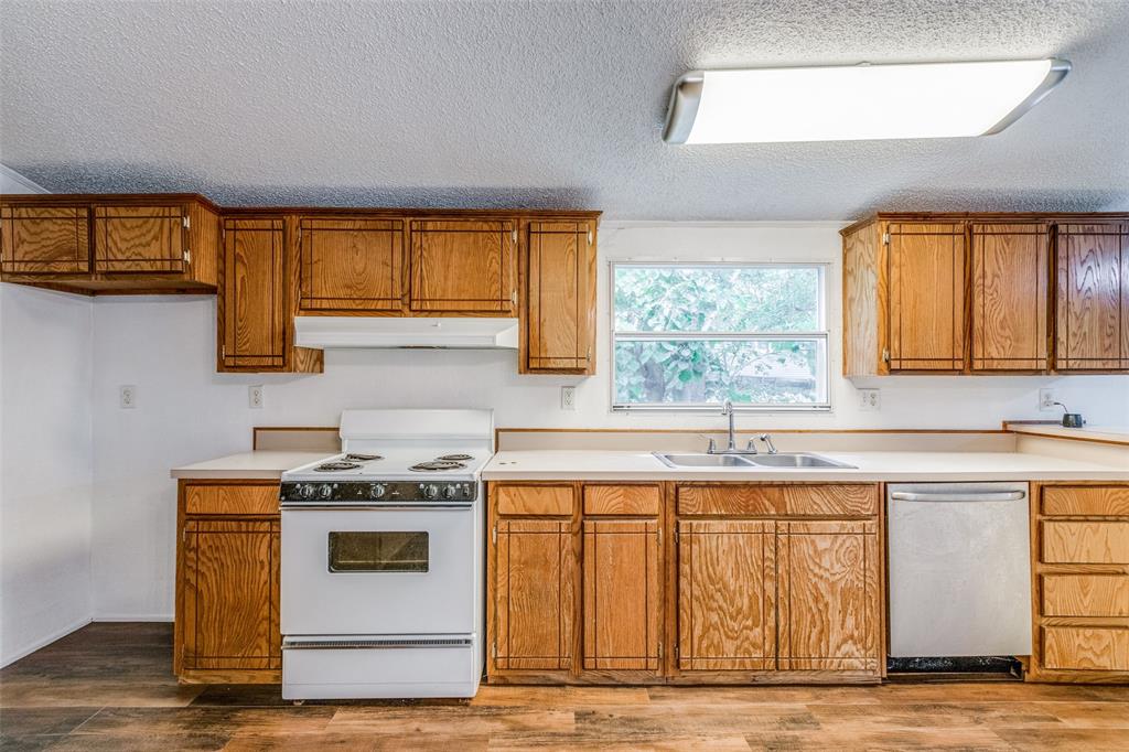 28 Wembley Road Gordonville, TX 76245 - Photo 6 of 24 Kitchen with space for a refrigerator, space for a range, stainless steel dishwasher, wood-type flooring, and a textured ceiling.