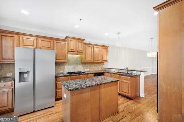 a kitchen with stainless steel appliances granite countertop a refrigerator a stove and a sink with wooden floors