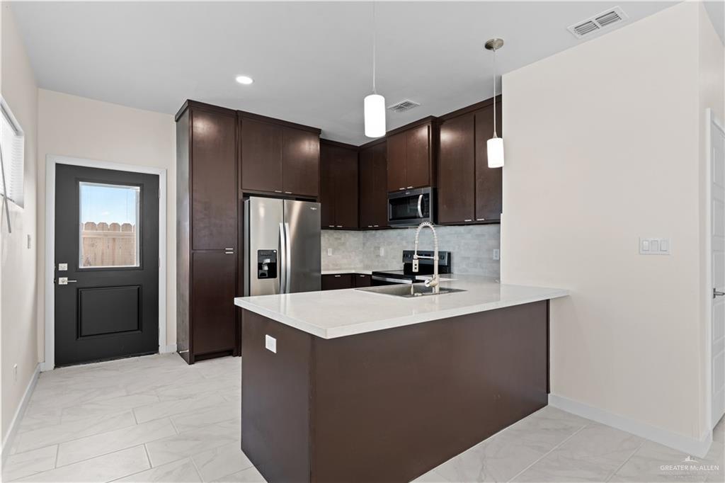 503 Sparrow Road Weslaco, TX 78596 - Photo 4 of 14 Modern kitchen featuring dark wood cabinetry, stainless steel appliances, a white solid surface countertop, and pendant lighting over a kitchen island