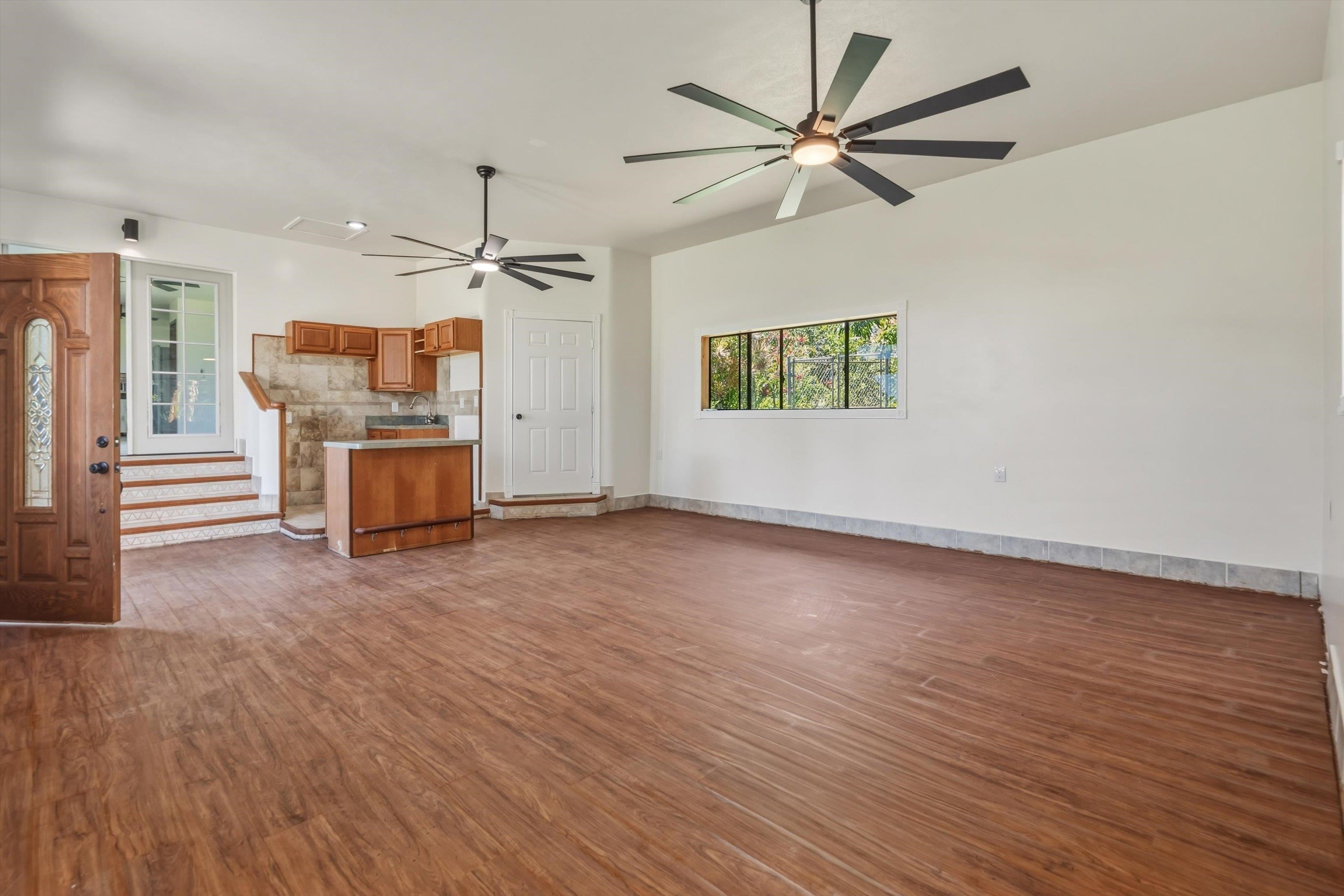 145 South Holokai Road Haiku, HI 96708 - Photo 7 of 50 an empty room with wooden floor a ceiling fan a fireplace and windows