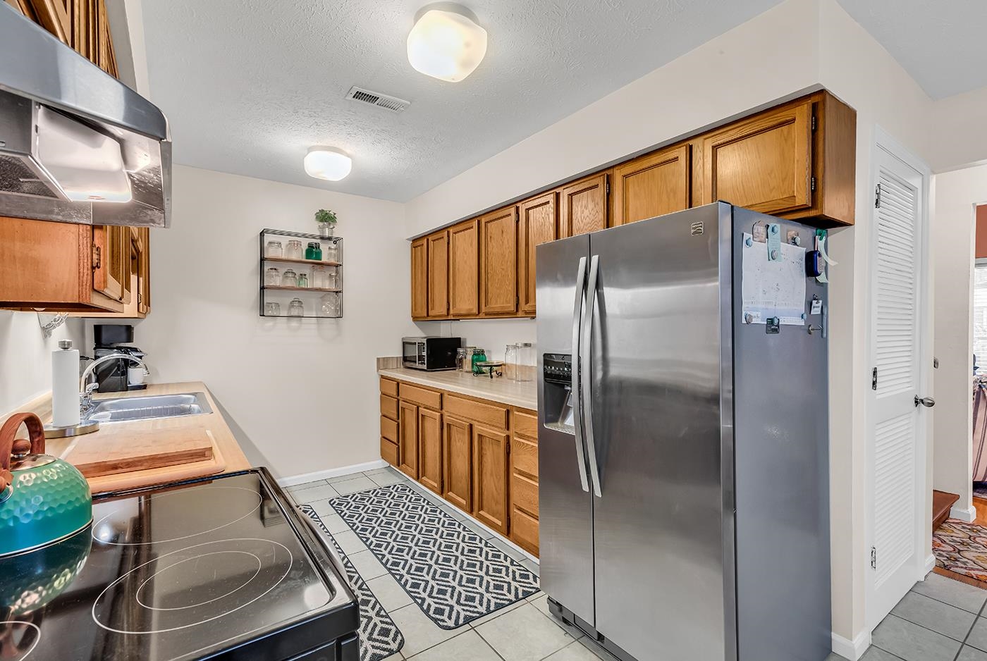 724 Juniper Drive, Unit B Surfside Beach, SC 29575 - Photo 11 of 36 Kitchen featuring appliances with stainless steel finishes, extractor fan, brown cabinetry, light countertops, and light tile patterned floors
