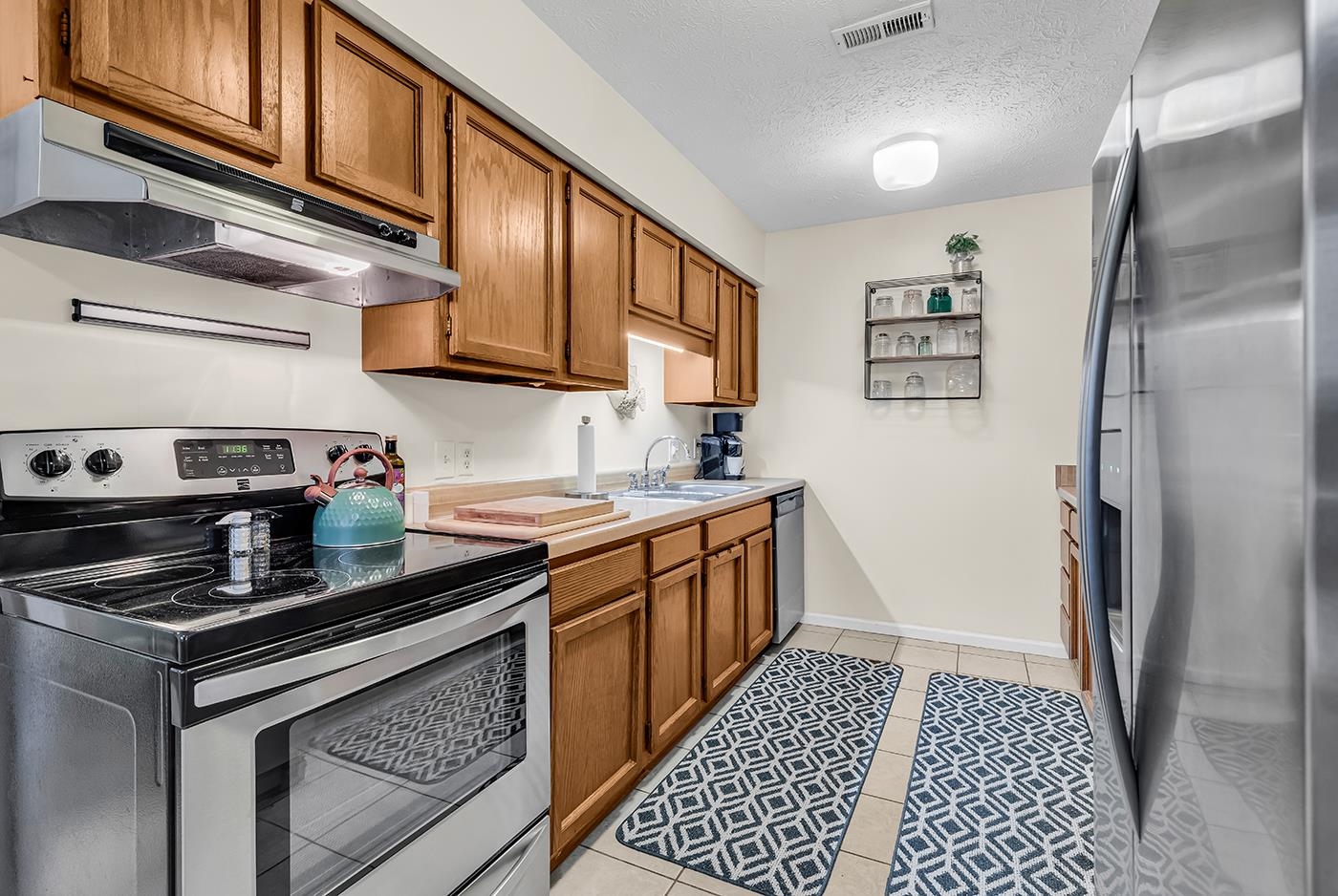 724 Juniper Drive, Unit B Surfside Beach, SC 29575 - Photo 9 of 36 Kitchen featuring stainless steel appliances, brown cabinets, under cabinet range hood, a textured ceiling, and light countertops