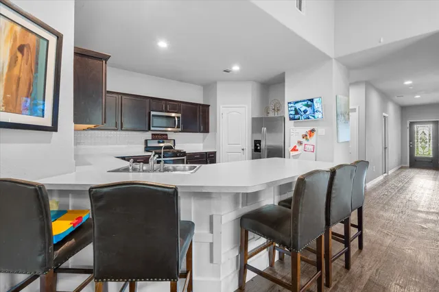 a kitchen with stainless steel appliances granite countertop a dining table chairs refrigerator and sink