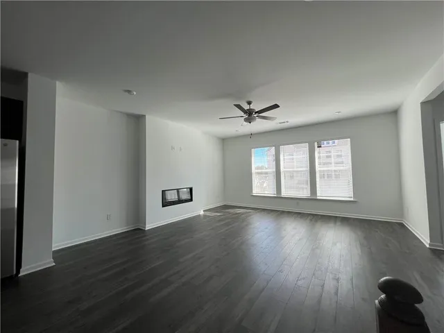 an empty room with wooden floor chandelier fan and windows