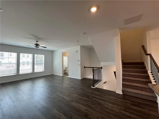 an empty room with wooden floor staircase and windows