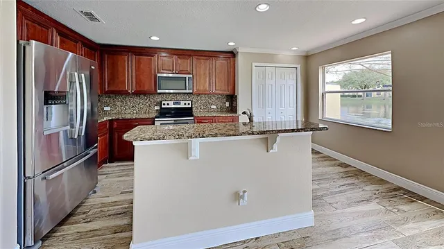 a kitchen with granite countertop stainless steel appliances a refrigerator microwave and wooden floor