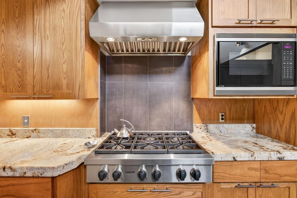 1080 North Greenbrier Road Nocona, TX 76255 - Photo 13 of 40 Stainless steel range with a professional-grade hood, natural wood cabinetry, stone countertops, integrated microwave, and a tiled backsplash