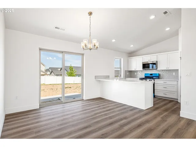 a view of an empty room and kitchen with wooden floor
