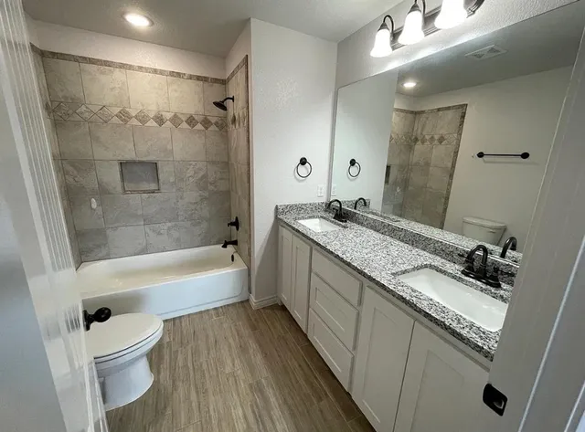 a bathroom with a granite countertop sink a toilet a mirror a bathtub and shower