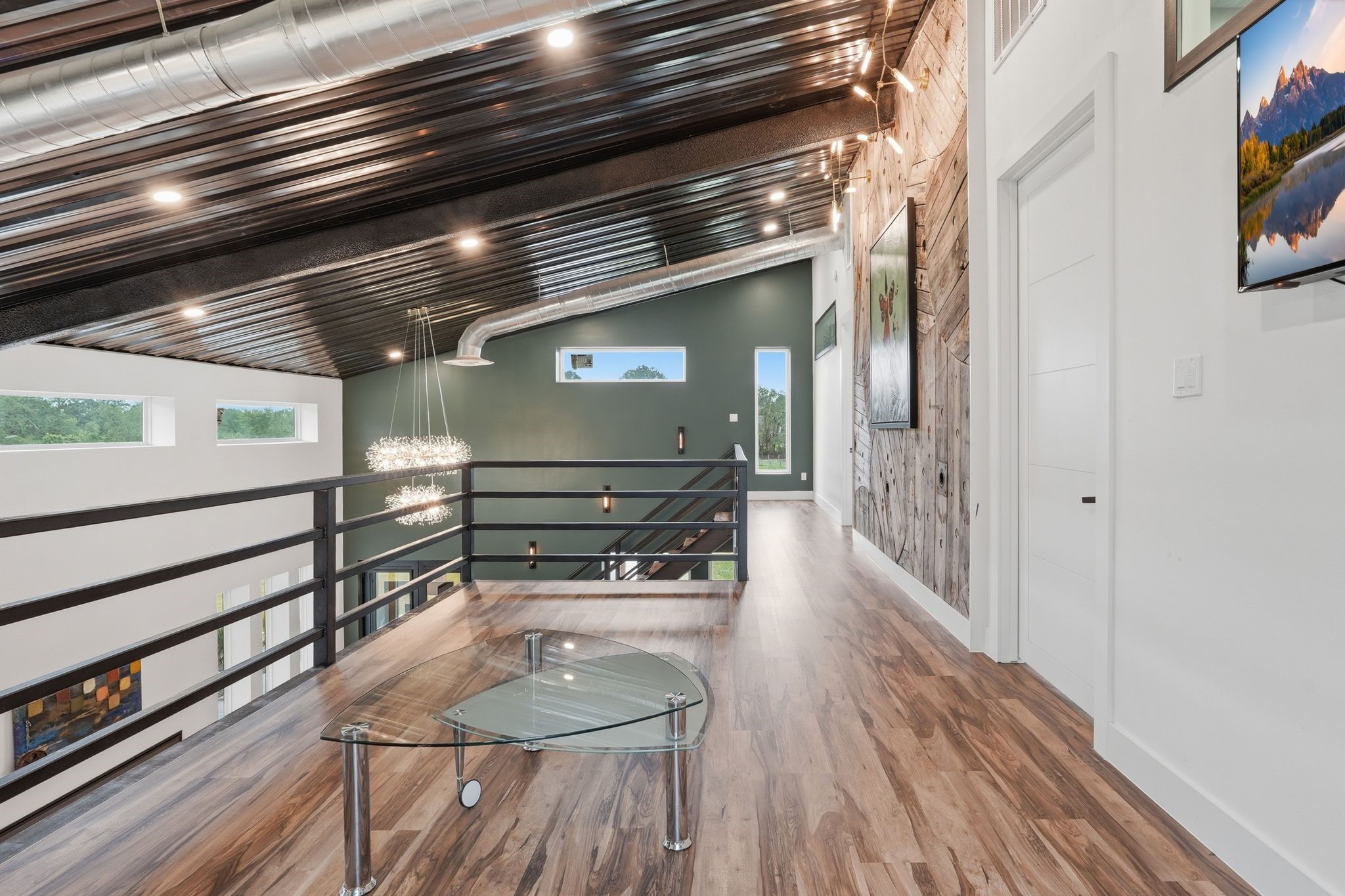2743 Bobville Road Montgomery, TX 77316 - Photo 43 of 50 This modern loft area features a sleek metal ceiling, exposed ductwork, and stylish wood flooring. Large windows offer natural light and views, while a glass coffee table and contemporary lighting enhance the space's elegance. Perfect for a creative workspace or relaxing retreat.