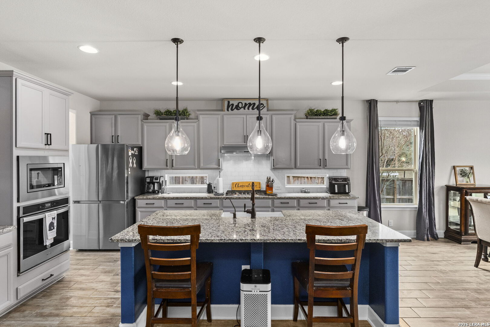 a kitchen with stainless steel appliances kitchen island granite countertop a dining table chairs and refrigerator