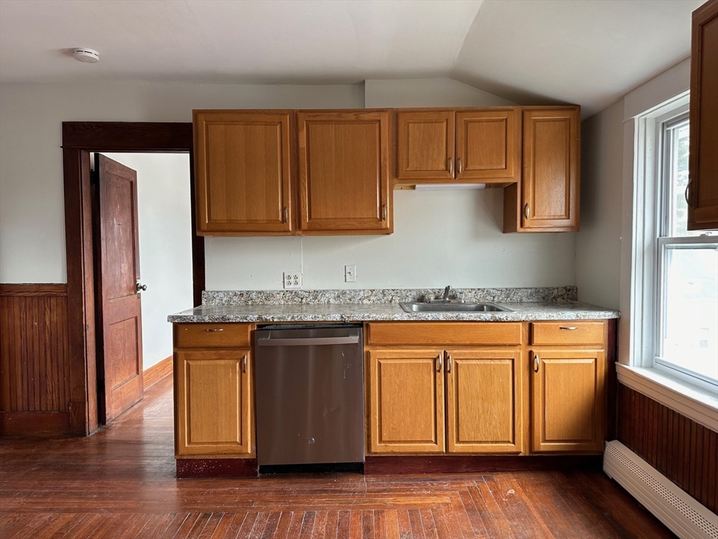 an open kitchen with granite countertop wooden cabinets a sink and dishwasher with wooden floor